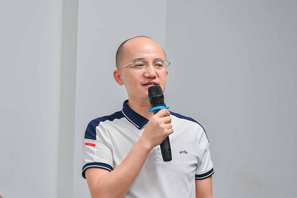 Gia Cát Duẩn cầm micro đang giảng, áo polo trắng