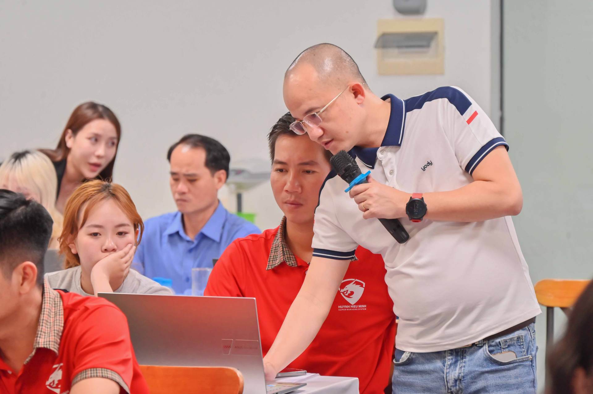 Gia Cát Duẩn cúi xuống kèm một học viên trên laptop, cả bàn cùng nhìn màn hình